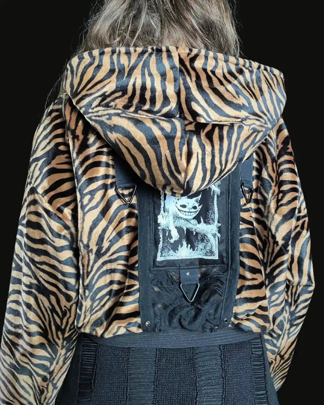Handgefertigte Tigerfell-Jacke aus veganem Kunstfell mit Kapuze und schwarzem Patch mit Grinsekatze-Print und Metallapplikationen am Rücken – Slow Fashion Darkwear von IUVA CRAFT STUDIO.