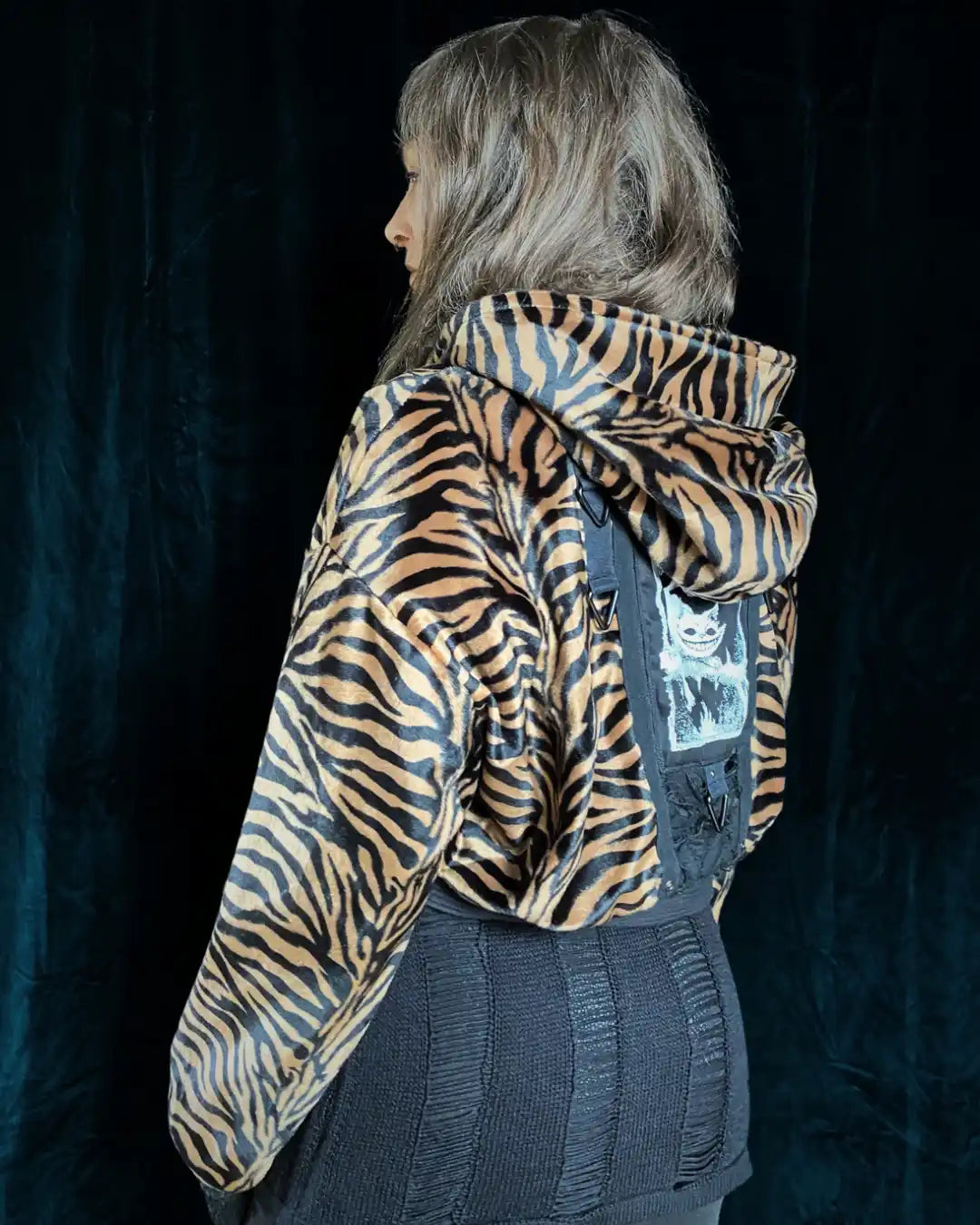 Vegane Tigerfell-Animalprint-Jacke mit schwarz-braunem Streifenmuster, breitem Bund, Kapuze, einzigartigem Rücken-Patch und Ringen – ideal für Darkwear-Looks und Clubstyles.