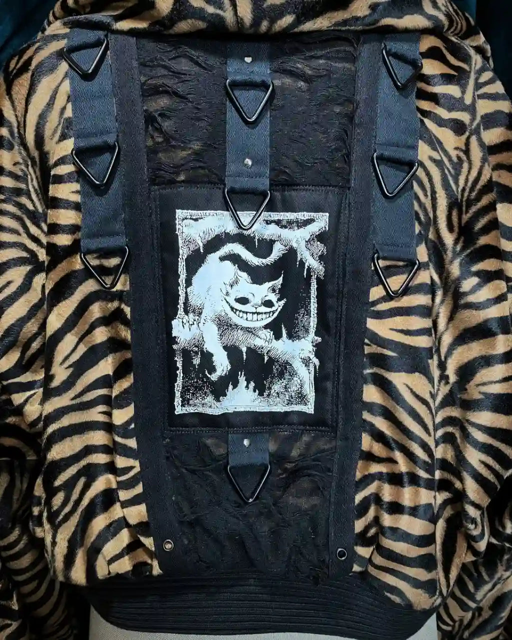 Handgenähte Festivaljacke im Tigerfell-Look, oversized geschnitten mit Kapuze und aufgenähtem Kunst-Print. Detailaufnahme Rücken mit Katzen.Patch, Netzstoff- und Metallapplikationen, Ringen und NIeten