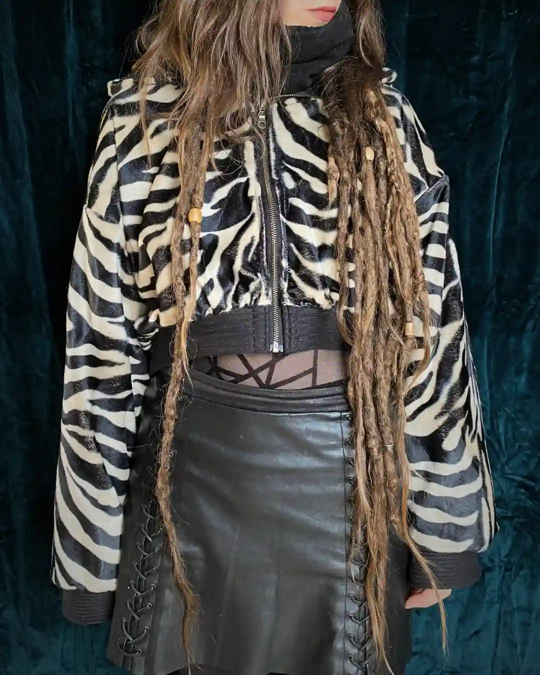 Zebra Felljacke aus Kunstfell von IUVA CRAFT STUDIO – handgefertigte kurz geschnittene Jacke im Darkwear-Stil mit schwarz-cremefarbenem Zebrastreifen-Muster, kombiniert mit schwarzem Lederrock und Mesh-Top. Zebra faux fur jacket by IUVA CRAFT STUDIO – handmade cropped jacket in darkwear style with black and cream zebra pattern, paired with black leather skirt and mesh top.