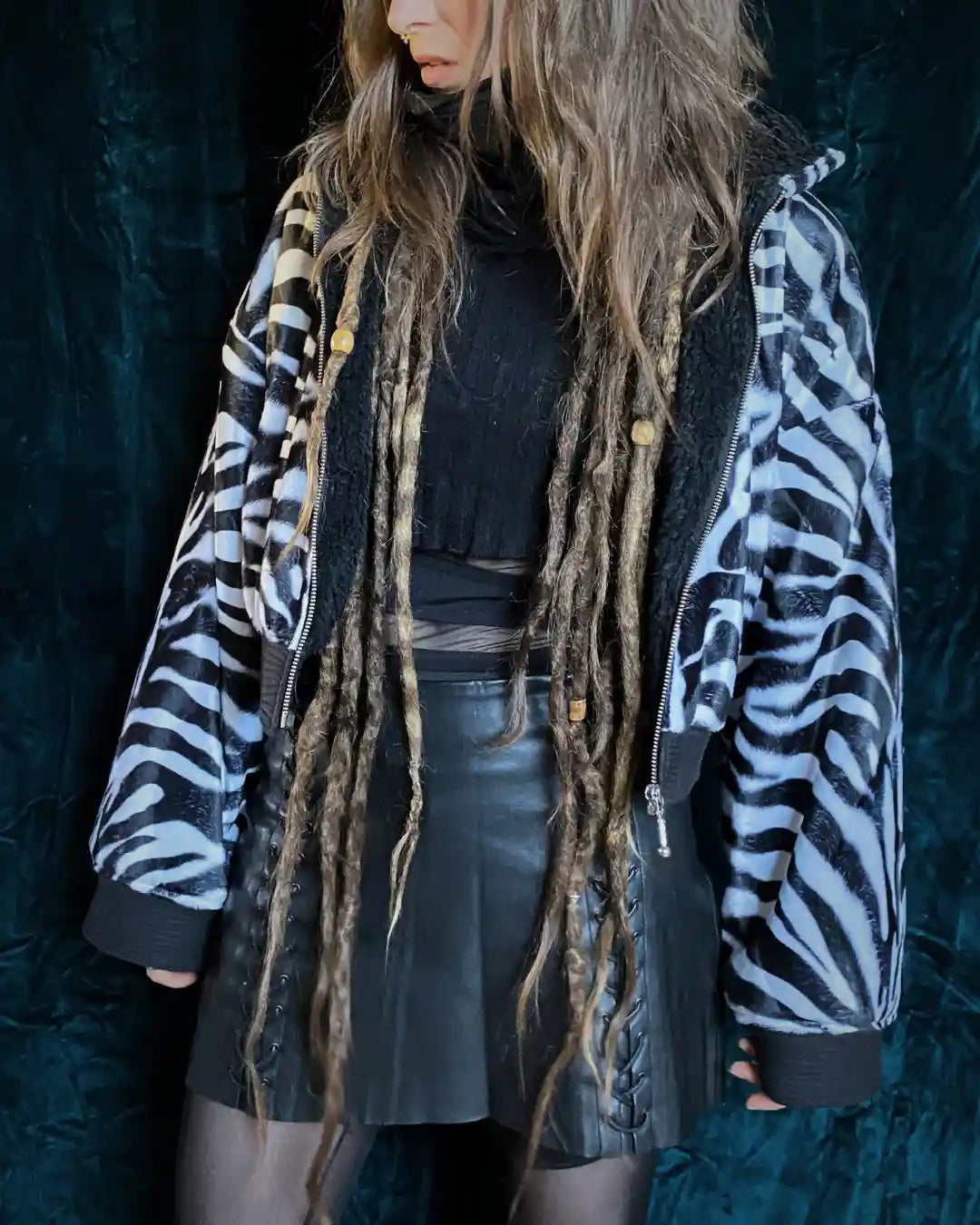Handgefertigte Zebra-Kunstfelljacke mit Kapuze, Reißverschluss und aufgenähtem Patch mit grafischem Augensymbol – Slow Fashion Darkwear von IUVA CRAFT STUDIO.